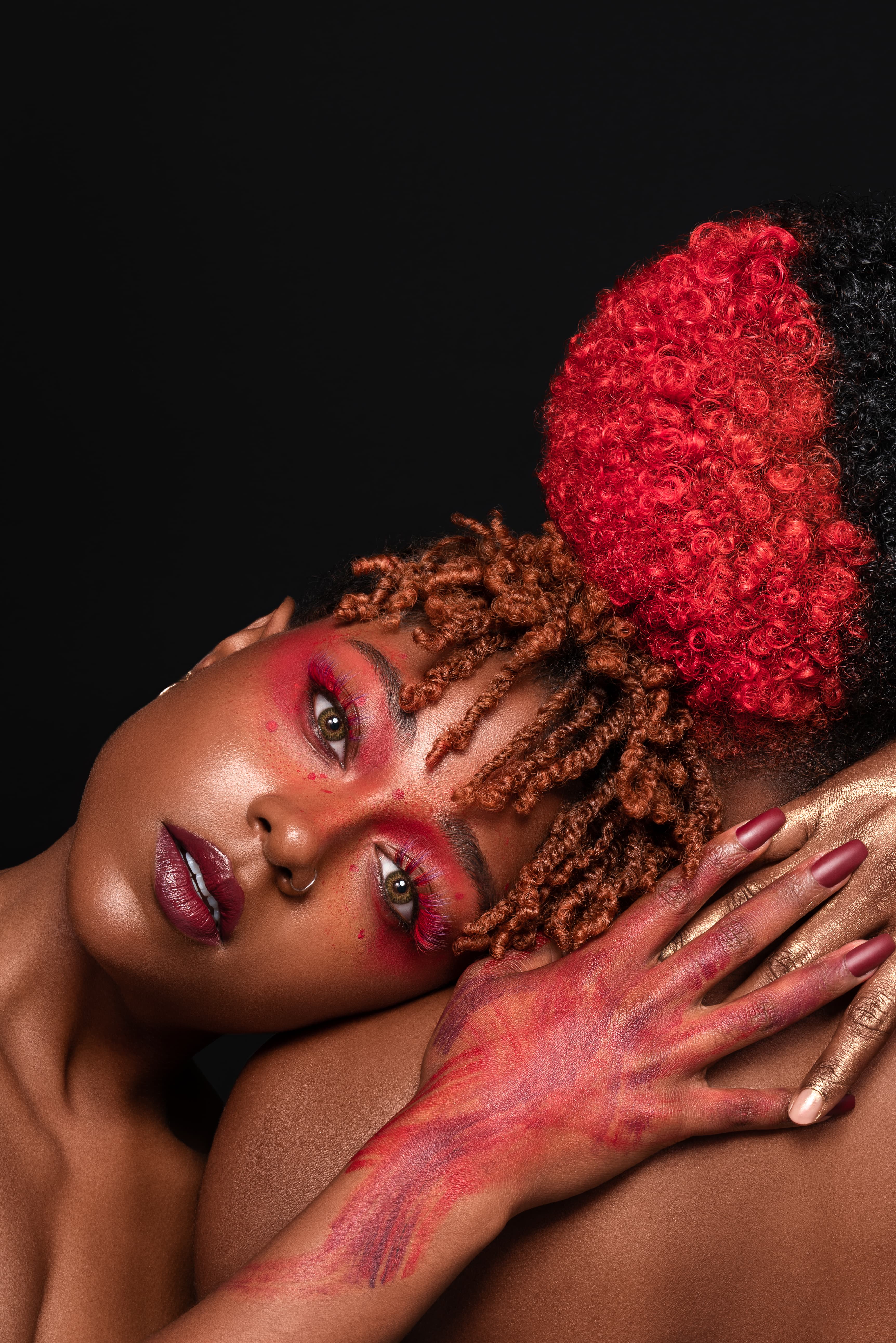 Close beauty portrait with bold red makeup and hands resting on a shoulder.